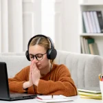 student online cute girl in glasses and sweater studying on computer praying